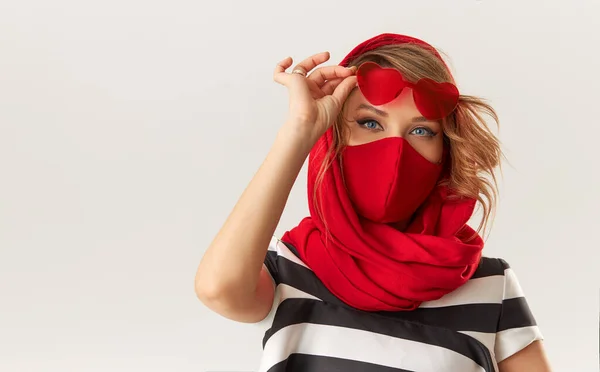 コロナウイルス感染症の隔離中に流行のファッションの服の女性 白い背景に保護スタイリッシュな赤い顔のマスクとハート型のサングラスのモデル — ストック写真