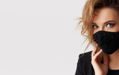 Coronavirus salgını karantinası sırasında modaya uygun giyinmiş bir kadın. Beyaz arka planda şık giyinmiş siyah koruyucu yüz maskesi