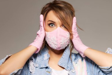 Surprised Woman in trendy fashion outfit during quarantine of coronavirus. Model dressed protective stylish pink face mask on  studio background