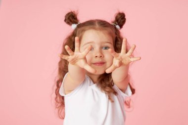 Pembe arka planda küçük şirin bir kızın şaşırmış portresi. Kameraya bakıyorum. Sol tarafı işaret eden eller. Çocuk ürünlerinin reklamını yapmak