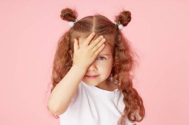 Pembe arka planda küçük şirin bir kızın şaşırmış portresi. Kameraya bakıyorum. Sol tarafı işaret eden eller. Çocuk ürünlerinin reklamını yapmak