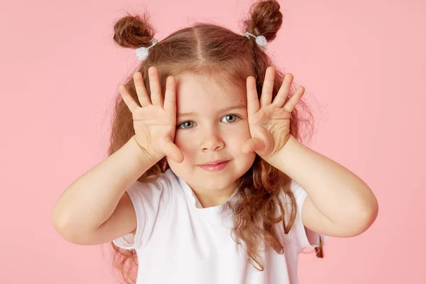 令人惊讶的可爱的小女孩的画像 背景是粉色的 看着摄像机 把手指向左边 儿童广告产品 — 图库照片
