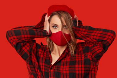 Fake news concept. Woman in trendy fashion outfit during quarantine of coronavirus outbreak. Model in protective handmade face mask and red beret covers ears from false news. 