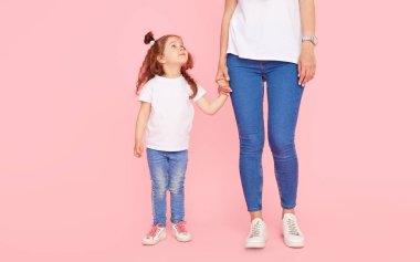 Aile değerleri. Beyaz tişörtlü ve kot pantolonlu anne ve kız pembe arka planda oynaşıp sarılıyorlar. Sevdiklerinle ilgilenmek. Mutlu annelik