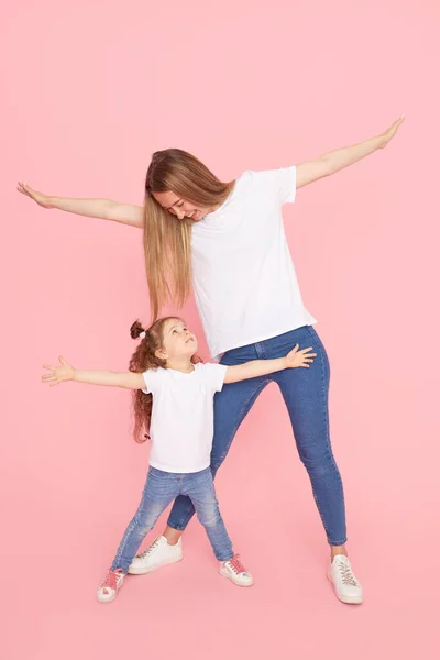 Aile değerleri. Beyaz tişörtlü ve kot pantolonlu anne ve kız pembe arka planda oynaşıp sarılıyorlar. Sevdiklerinle ilgilenmek. Mutlu annelik