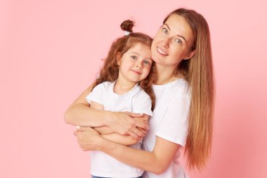 Beyaz tişörtlü ve kot pantolonlu anne ve kız pembe arka planda oynaşıp sarılıyorlar. Sevdiklerinle ilgilenmek. Mutlu annelik