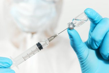 Biyolojik tehlike. Çin koronavirüsü salgını. Koruyucu giysili ve maskeli doktor şırınga ve aşı tutuyor. Grip aşısı, koronavirüs, ebola, tüberküloz. 