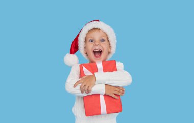 Noel Baba şapkalı küçük bir çocuğun portresi. Kahkahalar mavi arka planda izole. Hediye kutusu var. Yeni yıl tatiline hazırlanıyorum.