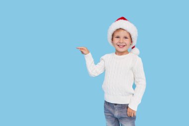 Noel Baba şapkası takmış küçük bir çocuğun portresi. Kahkahalar mavi arka planda izole. Sol tarafı işaret ediyor.