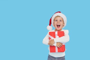 Noel Baba şapkalı küçük bir çocuğun portresi. Kahkahalar mavi arka planda izole. Hediye kutusu var. Yeni yıl tatiline hazırlanıyorum.