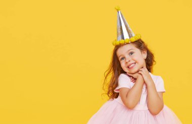 Parti zamanı. Şenlikli şapkalı, zarif elbiseli neşeli, küçük bir kız çocuğu doğum gününü sarı arka planda kutluyor. Metin için boş alan. Pankart