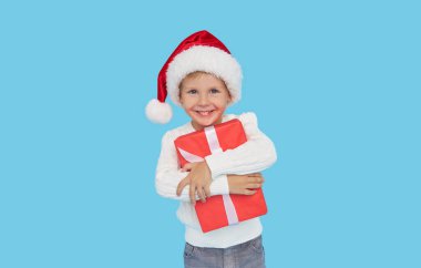 Noel Baba şapkalı küçük bir çocuğun portresi. Kahkahalar mavi arka planda izole. Hediye kutusu var. Yeni yıl tatiline hazırlanıyorum.