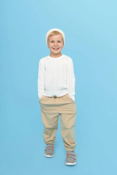 すごい顔だ 暖かい白い帽子と色の青の背景にセーターでかわいいスタイリッシュな小さなブロンドの男の子モデル 子供の販売と割引の冬の季節 — ストック写真