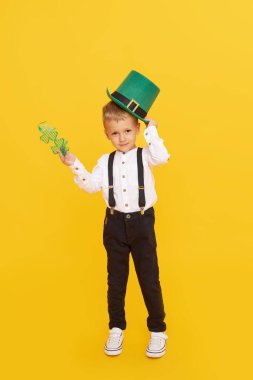 Smiling little child boy in green leprechaun hat on yellow background. St. Patrick Day celebration. Funny face clipart