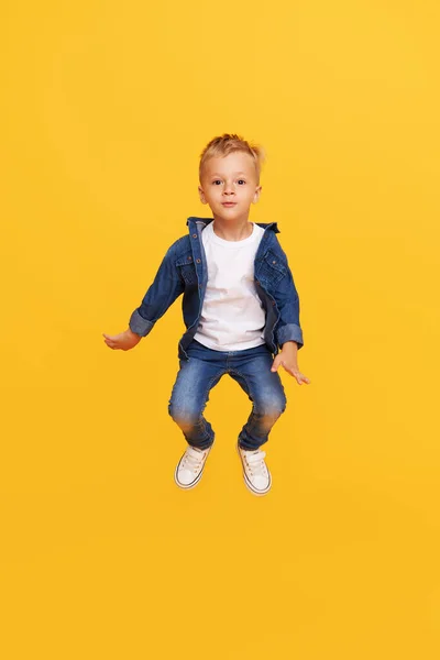 興奮した小さな男の子の完全な長さの肖像黄色の背景に隔離された喜びのためにジャンプ — ストック写真
