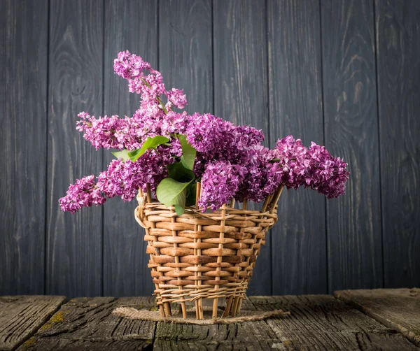 Cesta com um ramo de flor lilás em um fundo de madeira — Fotografia de Stock