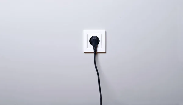 Toma de corriente eléctrica blanca y un cable de alimentación enchufado sobre fondo de pared blanco —  Fotos de Stock