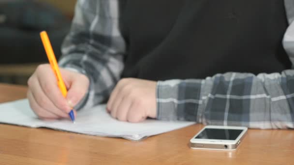 大学でのレッスンでデスクに座って黒いプルオーバーとシャツに灰色の未知の人は ノートにボールペンを使用してテキストを書き込みます 学生は 重要な情報のための銀の携帯電話 — ストック動画