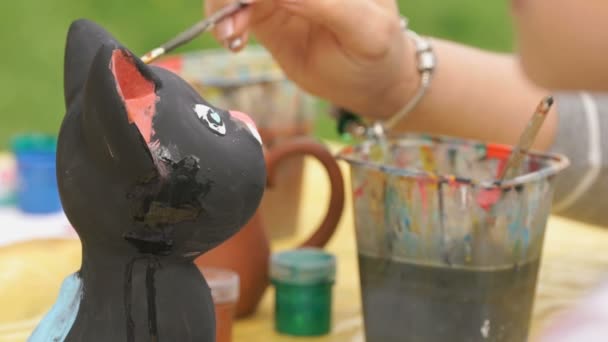 Child painting brushes on the clay figure outdoors — Stock Video