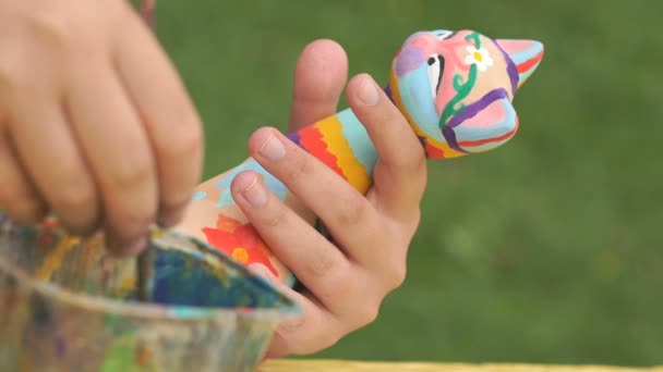 Child painting brushes on the clay figure outdoors — Stock Video