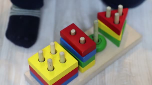 Ein einjähriges Kind legt geometrische Formen auf Stecknadeln in Holzkonstruktion. Nahaufnahme von Kinderhand und Spielzeug. — Stockvideo