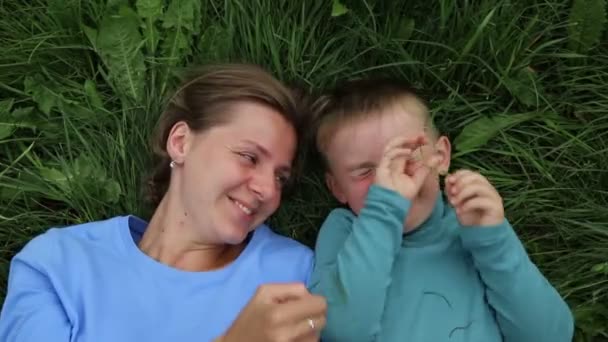 Madre e hijo yacen en la hierba y tontean, se divierten, ríen — Vídeo de stock