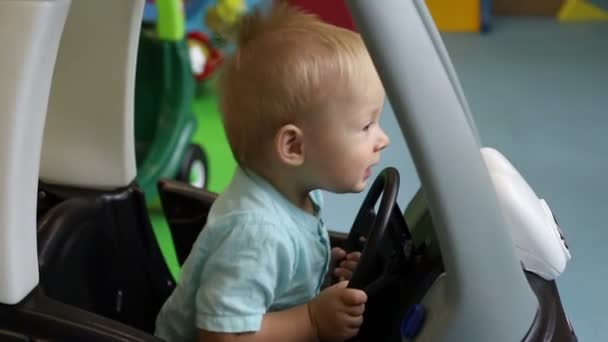 Slow Motion. Kind stuurders wiel in speelgoed auto. Kinder speelcentrum. Jongen rijdt speelgoed auto. — Stockvideo