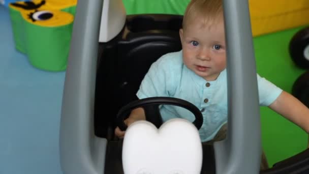 Baby drives toy car in children’s play center. Boy steers wheel. One year old child. — Stock Video