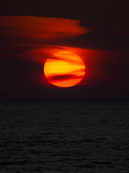 Siyah bulutlu büyük güneş, koyu turuncu bir günbatımı arka planı oluşturuyor..