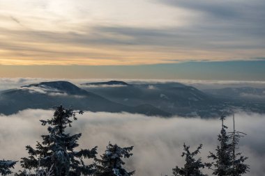 Smrk, Knehyne and Radhost hills from Lysa hora hill in winter Moravskoslezske Beskydy mountains in Czech republic with fog on lower altitudes and blue sky with clouds above clipart