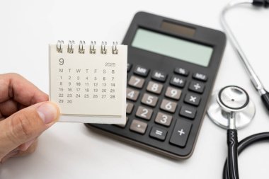 2025 Eylül takvimi, hesap makinesi ve stetoskop ile tıbbi randevu kavramı. Sağlık hizmetleri randevularını, sağlık kontrollerini ve hasta danışma programını sembolize eder.