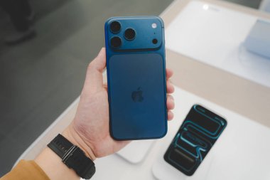 Hand holding a new Deep Blue iPhone 17 Pro Max in a Store.