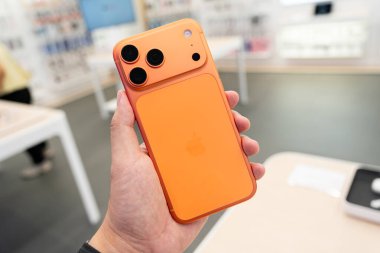 Hand holding a new Cosmic Orange iPhone 17 Pro Max in a Store.