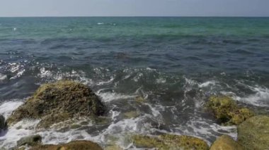 Deniz kıyısındaki kayalara çarpan güzel bir denizin mavi dalgalarını yakından çek..