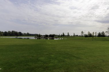  Geniş, mükemmel manikürlü yeşil çimlerin geniş bir manzarası. Geniş bir gökyüzünün altında, beyaz bulutlu bir gölet..