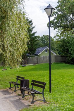 Ahşap banklar ve bir sokak lambası yemyeşil bir bahçede duruyor. Güzel bir kulübenin yanında. Huzurlu bir kaçış için mükemmel..