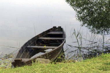 Sazlıklarla çevrili, çimli bir gölün kıyısındaki sakin suyun üzerinde eski bir ahşap tekne dinleniyor..