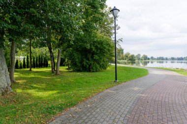 Sakin bir gölün yeşil kıyı şeridi boyunca kıvrımlı, asfalt bir yol esiyor, sokak lambası ve ağaçlarla kaplı..