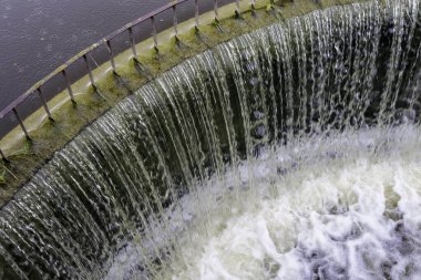 Çembersel bir sızıntının üzerine dökülen su, yağmurlu bir günde aşağıda küçük bir şelale ve köpüklü bir havuz oluşturuyor..