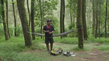 Bir hamakta dinlenerek çam ormanının güzel doğal atmosferinin tadını çıkarıyorum. Doğada tek başına sakin bir hayatın tadını çıkar.