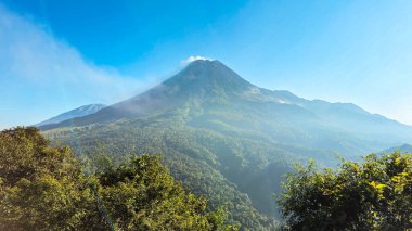 Sabah Merapi Dağı manzarası ve önü yemyeşil bir orman. Açık bir sabahta Merapi Dağı 'nın panoramik güzelliği belli bir mesafeden görülebiliyor..