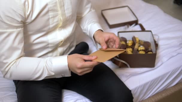 Un hombre se sienta en una cama en hoteles y lee una carta de un sobre — Vídeos de Stock