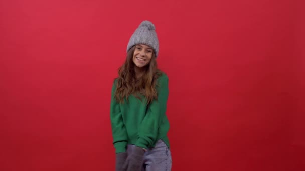 Дівчина в зеленому светрі з капелюхом на червоному тлі — стокове відео
