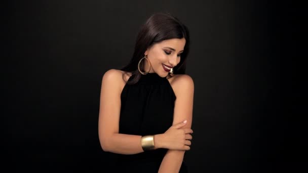 Girl with bright dark make-up poses for the camera on a black background in black clothes with gold earrings — Stock Video