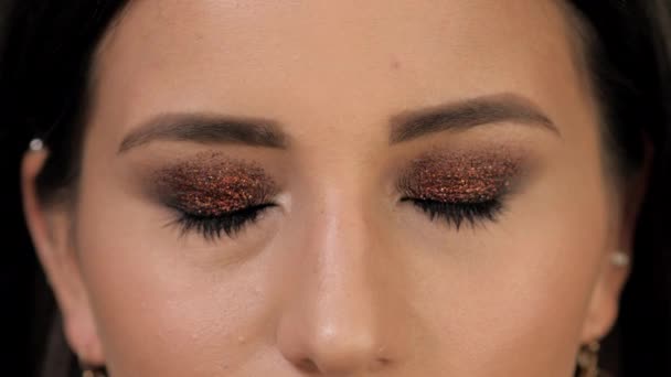 En tjej med ljus makeup och gnistrar i hennes ögon öppnar ögonen för kameran. Närbild shot — Stockvideo