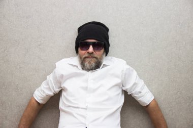 Gözlüklü sakallı ve şapkalı gömlekli bir adam çanta tutuyor..