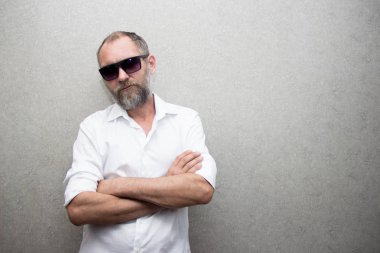 Gözlüklü sakallı gömlekli bir adam kolları çapraz duruyor..