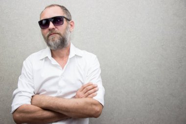 Gözlüklü sakallı gömlekli bir adam kolları çapraz duruyor..