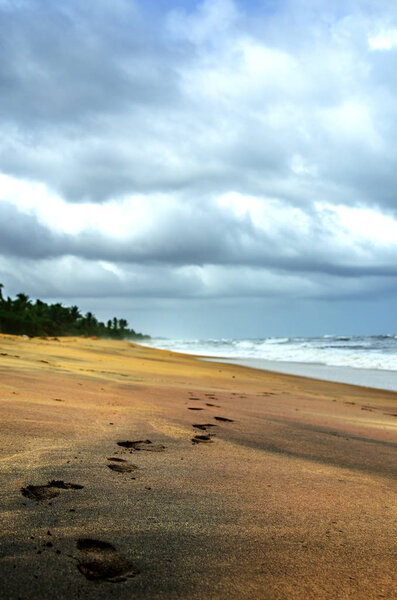 Footprints on a deserted beach in Sri Lanka. Above the stormy ocean, a gloomy cloudy sky with heavy clouds.