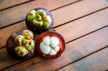 Olgun kesim ve ahşap bir masa üzerinde iki bütün mangosten.